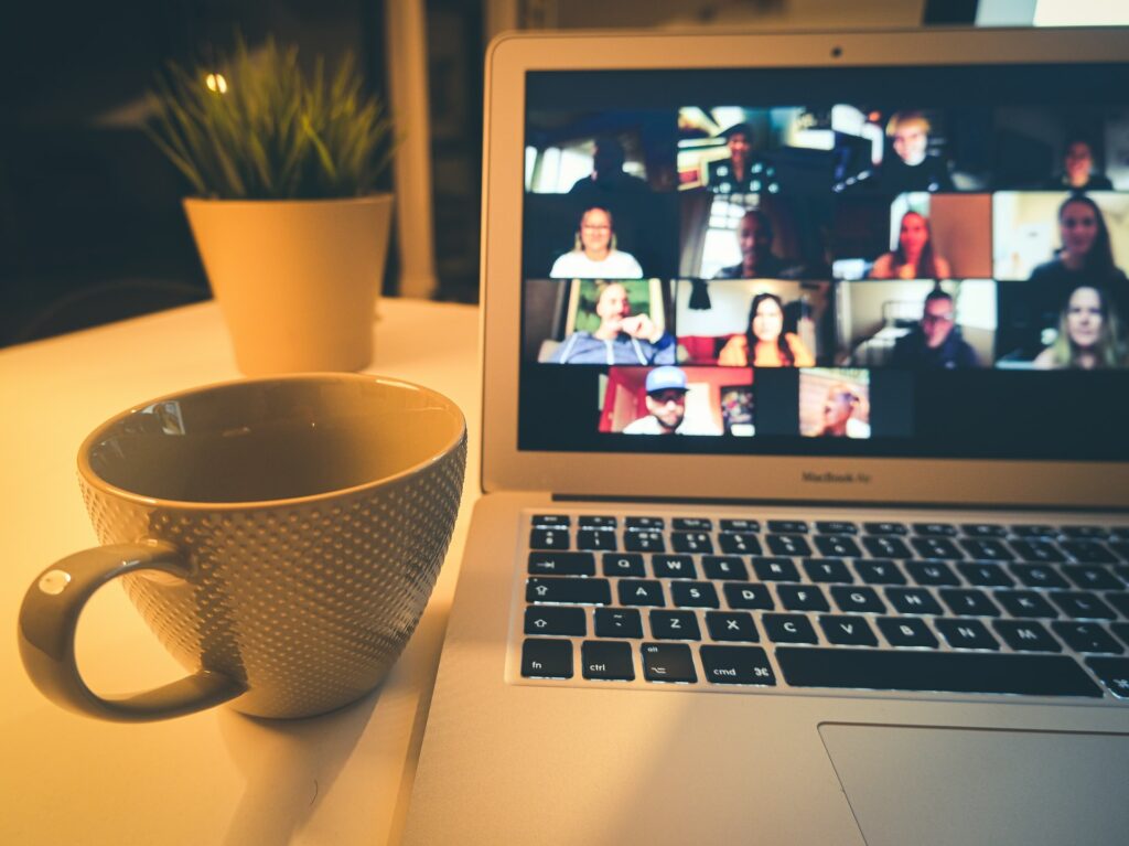 A laptop next to a coffee mug on a desk with a small plant on it. The laptop is showing a zoom call which background removal could be a good work from home upgrade.