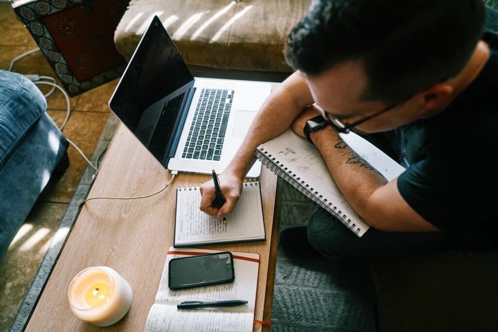 A person is sat at a kitchen table making notes in a notebook, something you should do after you stream.