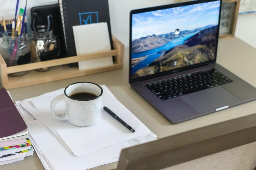 A laptop on a desk next to a notepad and a cup of coffee ready to make a remote pitch