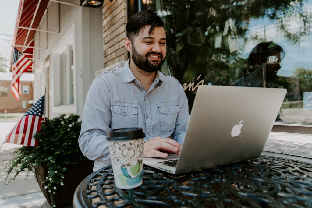 A person sat outside a cafe using a laptop to watch a pre recorded meeting to save time at work.