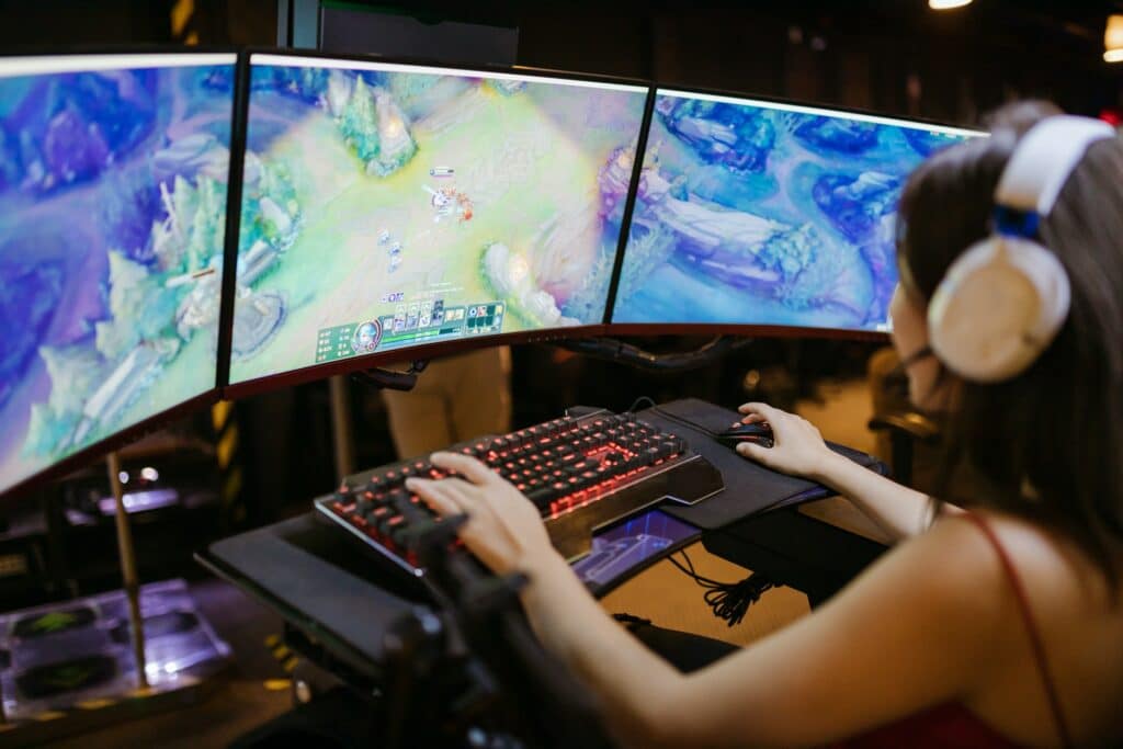 A person playing a game across three monitors with a gaming headset on facing the screens wondering how to stream a vtuber.