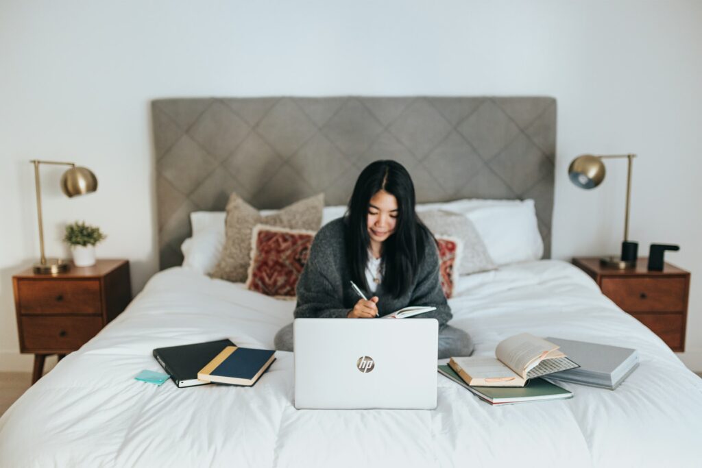 A person sits at their laptop, surronded by notebooks as they themselves make notes in preparation for an online presentation. 